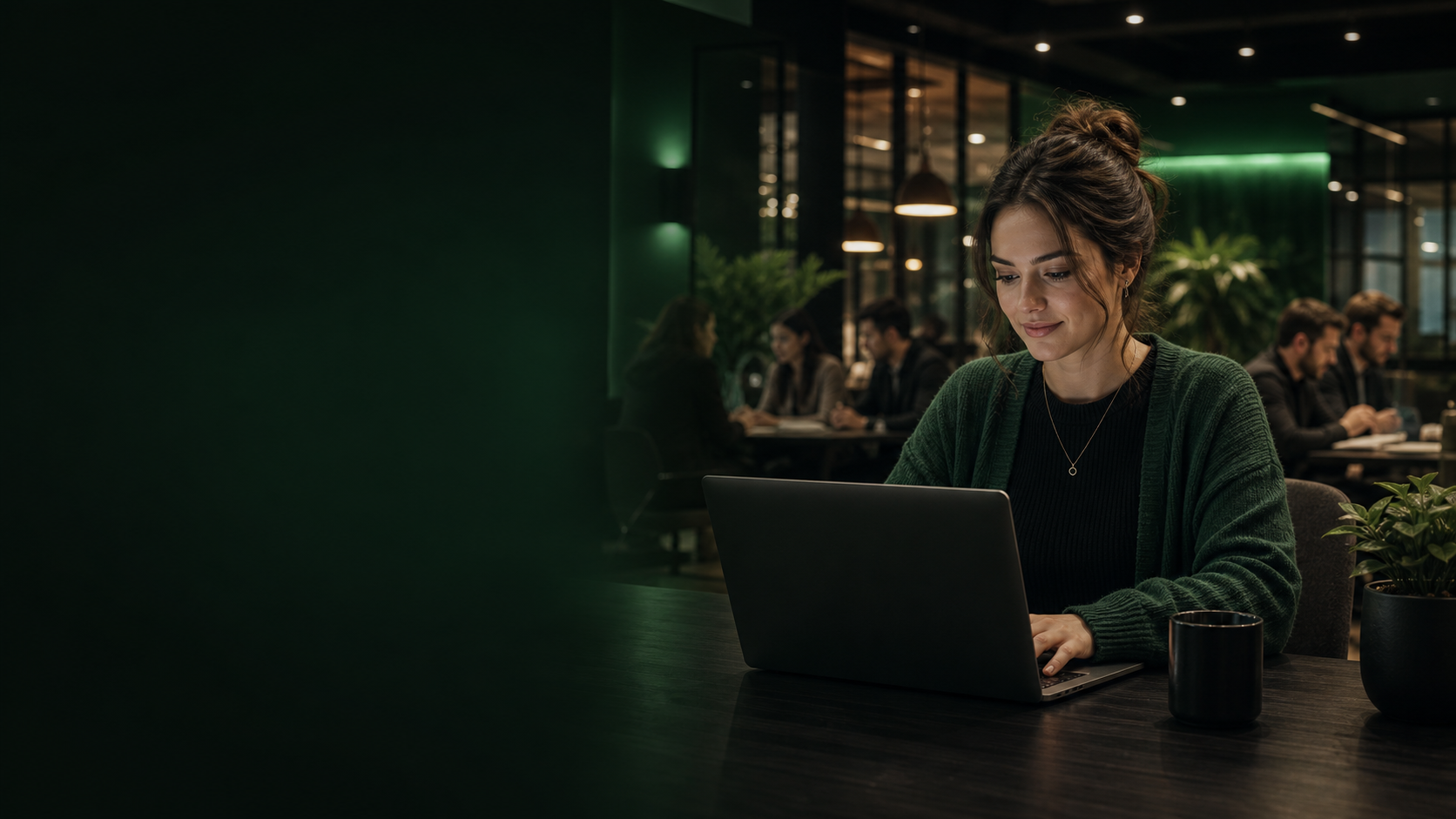 Woman working on a laptop in a dark emerald coworking space